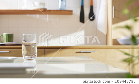 A sunny kitchen with white tile walls, a wooden table and sink. 109443783