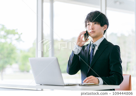 Young Asian businessman using a computer while talking on his smartphone 109444806