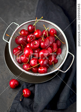 Ripe sweet cherry berry with leaves in a pan on a black wooden board Ripe sweet cherry berry with leaves in a pan on a black wooden board 109444848