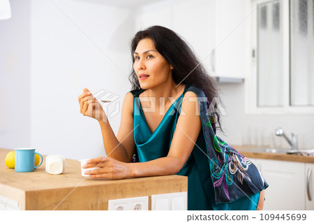 Portrait of woman eating yoghurt at home 109445699