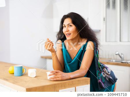 Portrait of positive woman in nightdress eating yogurt at home Portrait of positive woman in nightdress eating yogurt at home 109445710