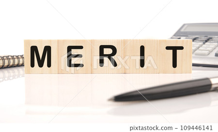 Merit word assembled from wooden cubes next to a calculator, pen and notepad Merit word assembled from wooden cubes next to a calculator, pen and notepad 109446141