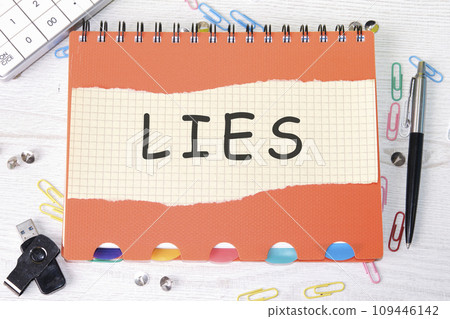 Lies word is written on a sheet in a cage lying on a notebook on the table next to stationery 109446142