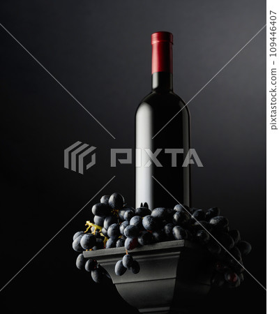 Blue grapes and a bottle of red wine on a black background. 109446407