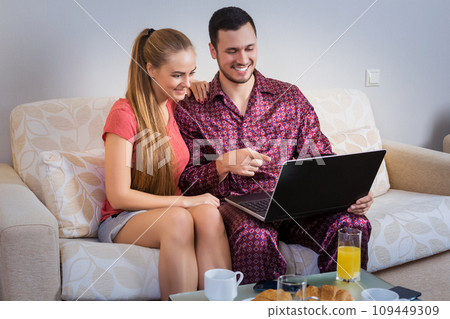 Cute young couple having breakfast, in front of laptop computer Cute young couple having breakfast, in front of laptop computer 109449309