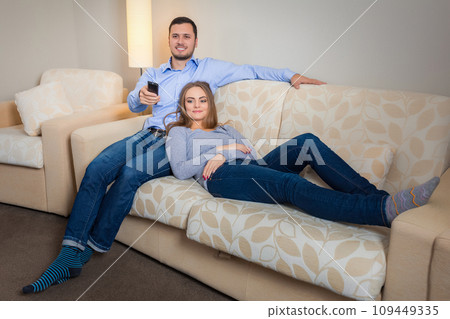 Portrait of happy couple sitting on sofa watching television together Portrait of happy couple sitting on sofa watching television together 109449335