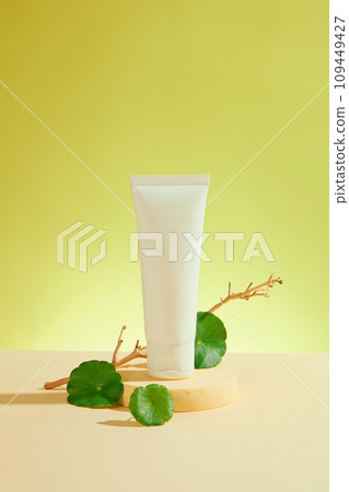 Front view of mockup container for moisturizing cream or cleanser, beauty cosmetics with gotu kola leaves decorated on green background. Advertising photo, natural gotu kola extract 109449427