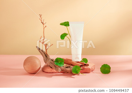 Mockup scene for advertising organic cosmetic with ingredient from gotu kola. A white plastic tube decorated with fresh centella leaves, cinnamon stick and dry twig decorated on beige background 109449437