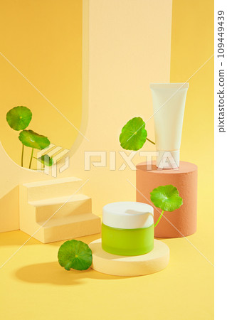 On a yellow background with beige props and fresh gotu kola leaves, set of cosmetic with tube and jar displayed. Minimal mockup for design. Beauty herbal skincare and haircare concept. 109449439