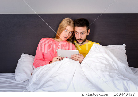 Young Sweet Couple at Bed Watching Something on Tablet Gadget 109449458