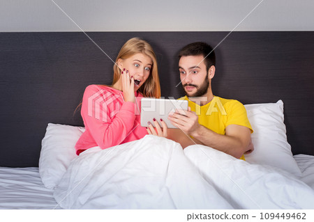 Young Sweet Couple at Bed Watching Something on Tablet Gadget Young Sweet Couple at Bed Watching Something on Tablet Gadget 109449462