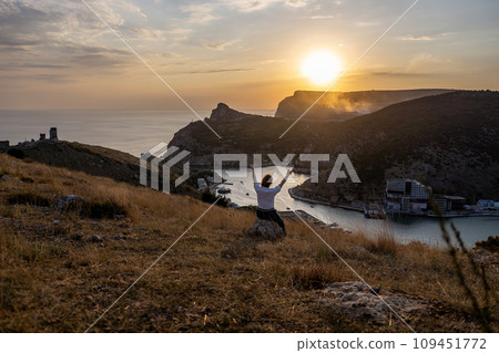 Happy woman on sunset in mountains. Woman siting with her back on the sunset in nature in summer with open hands. Silhouette. 109451772