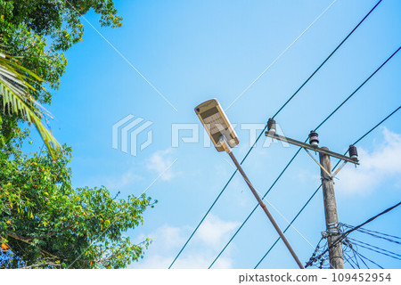 The street lamp sits on a wooden pole next to the power line. The light is bright and shining, and power lines are visible in the background. The street lamp sits on a wooden pole next to the power line. The light is bright and shining, and power lines are visible in the background. 109452954