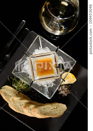 Pike fish caviar, on ice, with croutons, lemon, on a transparent dish, on a dark background 109453046