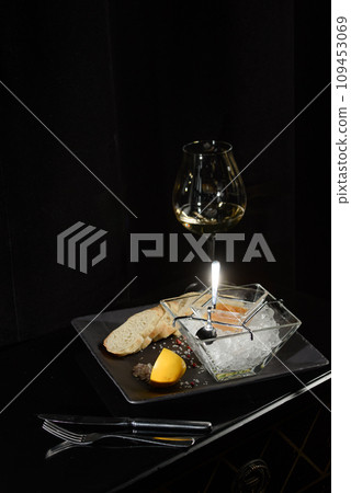 Pike fish caviar, on ice, with croutons, lemon, on a transparent dish, on a dark background 109453069