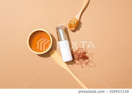 Unlabeled bottle decorated with a bowl of honey, saffrons and beeswax on a spoon. Mockup of skin care cosmetic bottle of beauty facial with honey extract  109453130