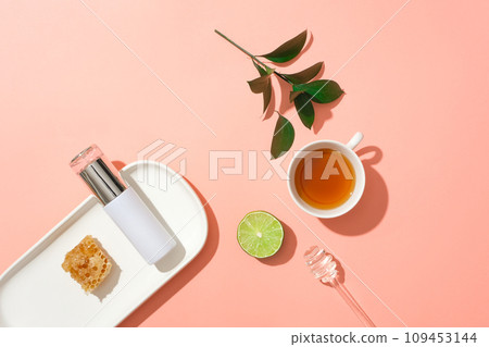 A dish featured a cosmetic bottle and beeswax. A teacup, lime slice and honey dripping displayed. Honey is a sticky and sweet substance 109453144