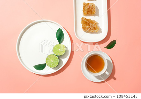 Few slices of lime, beeswax and a teacup arranged on white dishes. Empty space for natural beauty product promotion of Honey extract Few slices of lime, beeswax and a teacup arranged on white dishes. Empty space for natural beauty product promotion of Honey extract 109453145