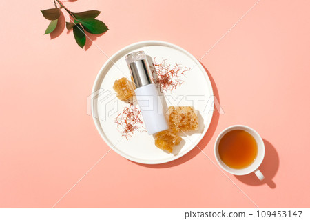 Empty label bottle decorated with saffrons and beeswax on a dish. Green leaves and a cup of tea featured. Blank label for branding mock-up 109453147