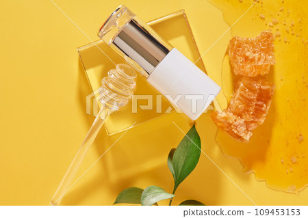 Cosmetic bottle decorated with a honey dripping on glass podium. Honey and beeswax featured on yellow background. Branding mockup of Honey extract 109453153