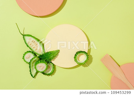On a green background with color podiums, fresh bitter melon slices decorated. Blank space for display product. Vitamin E in the bitter gourd mask helps to hydrate and soften the skin 109453299