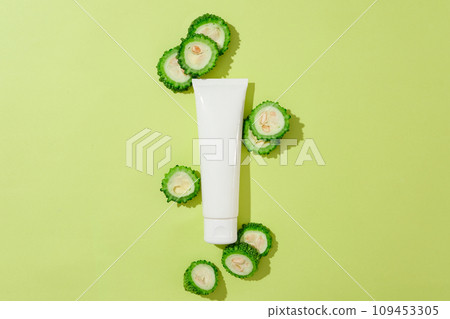 Top view of bitter slices decorated with cosmetic bottle unbranded on green background. Mockup for design and advertising cosmetic of bitter melon extract. Space for design Top view of bitter slices decorated with cosmetic bottle unbranded on green background. Mockup for design and advertising cosmetic of bitter melon extract. Space for design 109453305