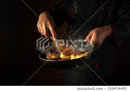 The chef fries dough donuts in a frying pan. Place for hotel menu or recipe on black background The chef fries dough donuts in a frying pan. Place for hotel menu or recipe on black background 109454491