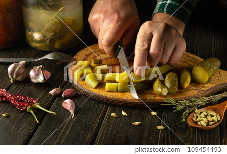 The process of preparing a delicious dish with pickles for lunch. The chef cuts a pickled cucumber into small pieces with a knife. Work environment on kitchen table with spices and seasonings 109454493