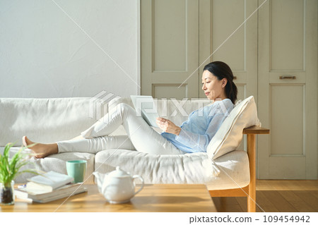 A woman lying on the sofa and working on a computer A woman lying on the sofa and working on a computer 109454942