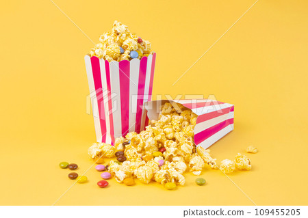Two striped carton buckets with caramel popcorn and dragee candies on yellow background 109455205