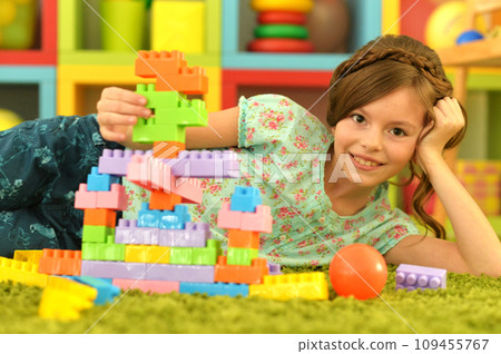 Portrait of cute girl playing with colorful plastic blocks in room 109455767
