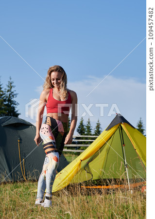 Woman hiker camping in mountains. Woman wearing sportswear, traveling, hiking outdoors. Pretty, young female posing, smiling, having break. Concept of harmony with nature. 109457482