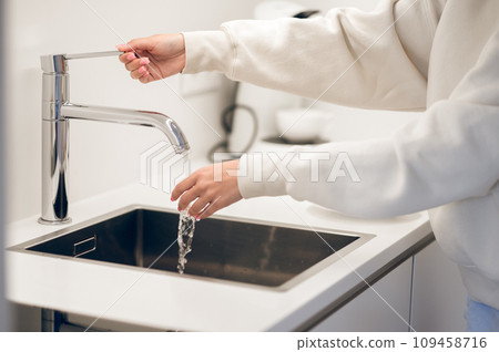 Girl in white hoodie standing near the kitchen sink in the kitchen Girl in white hoodie standing near the kitchen sink in the kitchen 109458716