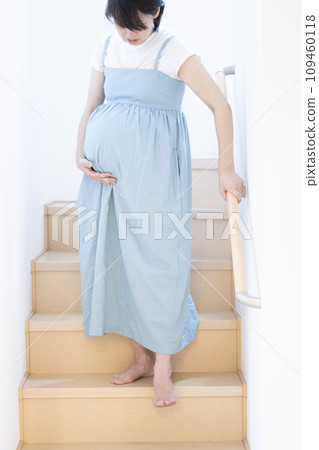 A pregnant woman at full term descending the stairs carefully 109460118