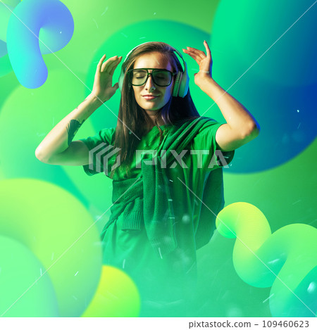 Calm and joy. Attractive young lady dancing, smoothly moves during listening music radiating positive energy against abstract background in green neon light. Calm and joy. Attractive young lady dancing, smoothly moves during listening music radiating positive energy against abstract background in green neon light. 109460623