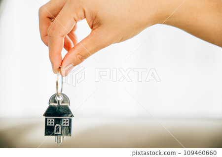 Hand holds house key marking homeowners' achievement. Agent presents model home symbolizing real estate success. Confidence and happiness shine. 109460660
