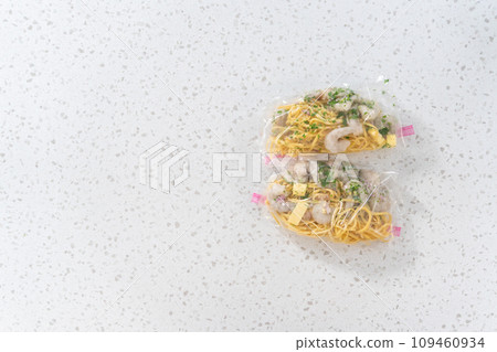 Flat lay. Packaging homemade frozen shrimp scampi meal prep into plastic resealable bags. 109460934