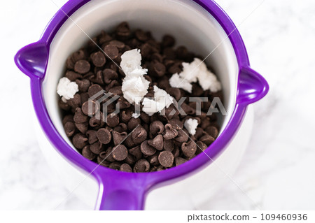 Melting chocolate chips in a candy melting pot to make chocolate icing for panda-shaped shortbread cookies. 109460936
