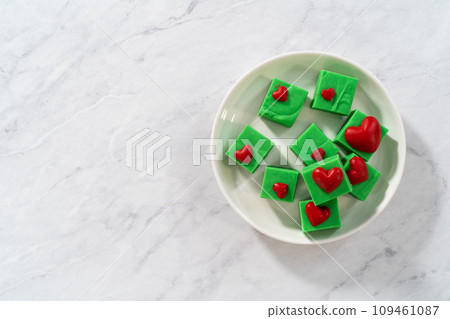 Homemade chocolate green fudge with red hearts square pieces on a white plate. 109461087