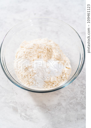 Mixing dry ingredients with a hand whisk in a large glass mixing bowl to bake banana cookies with chocolate drizzle. Mixing dry ingredients with a hand whisk in a large glass mixing bowl to bake banana cookies with chocolate drizzle. 109461123