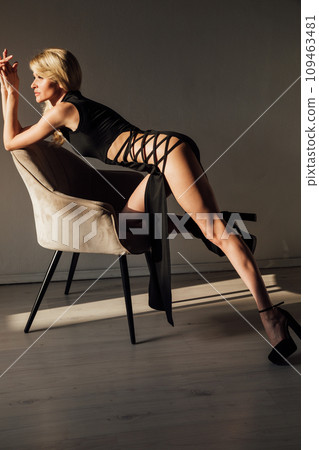 Beautiful blonde woman in black tight evening dress sitting in armchair 109463481