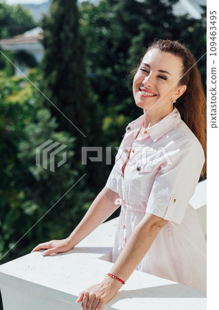Beautiful woman in summer light dress on balcony looking at the street Beautiful woman in summer light dress on balcony looking at the street 109463495
