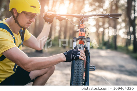 Man cheching tire pressure on bicycle wheel during ride in forest 109464320