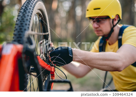 Cyclist checking chainwheel defect on upside down bicycle in forest 109464324
