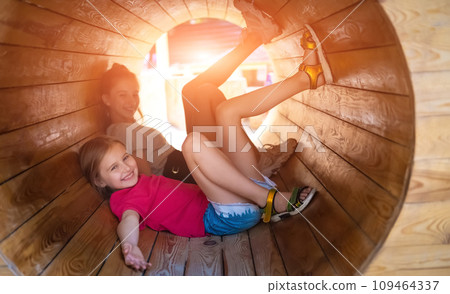 Smiling children lying in wooden tube on sunny playground 109464337