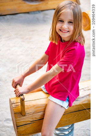 Happy little girl riding wooden swing on kids playground 109464339