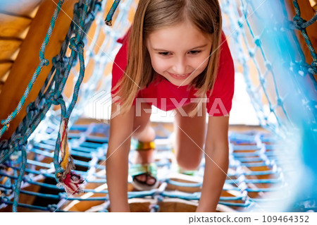 Little girl climbing throught net on playground in park 109464352
