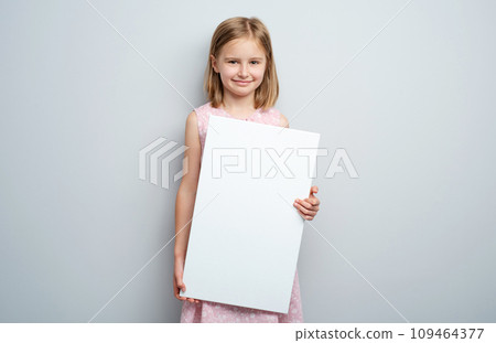Little girl holding vertical empty placard on gray wall background 109464377