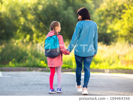 Rear view of mother and schoolgirl holding hands walking along car parking Rear view of mother and schoolgirl holding hands walking along car parking 109464398