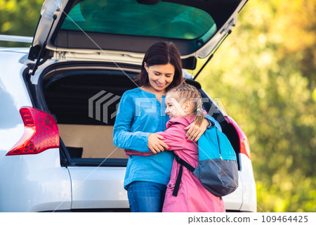 Mother hugging little girl after school next to open car trunk Mother hugging little girl after school next to open car trunk 109464425
